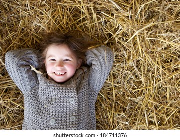 Close up portrait of a cute little girl smiling and lying down on hay. Fun and relaxing