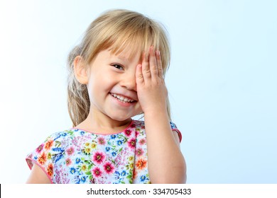 Close Up Portrait Of Cute Little Girl Closing One Eye With Hand Against Blue Background.