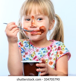 Close up portrait of Cute little girl eating chocolate yogurt at breakfast. Face messy with chocolate and naughty facial expression.