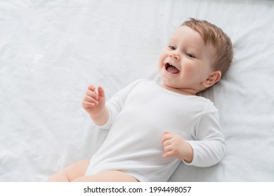 Close Up Portrait Of A Cute Little Small Child Caucasian Infant Toddler Newborn Smiling With Baby Milk Teeth Lying On The Comfortable Bed. Teething Concept, Childcare And Parenthood.