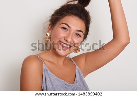 Close up portrait of cute and smiling lady with dark wavy hair, young girl with pony tail looking directly at camera, adorable woman wearing grey casual t shirt isolated over white studio background.