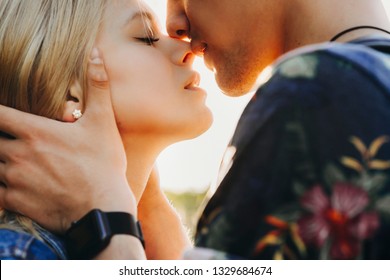 Close up portrait of a cute young caucasian blonde couple trying to kiss where man is holding his girlfriend face in his hands close outside while dating.