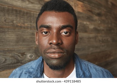 Close up portrait of dark-skinned man looking seriously at camera on wooden background. Thoughtful and peaceful facial expression, relaxed and regular mimics of African person with little beard. - Powered by Shutterstock