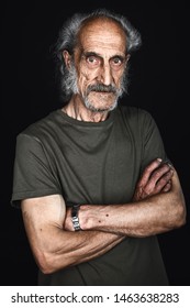 Close Up Portrait Of Elderly Sick Man In Green T-shirt With Crossed Arms Posing To The Camera In Black Background. Studio Shot.tiredness,studio Shot.