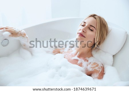Close up portrait of elegant blonde Caucasian woman closing her eyes while resting in the hydro bath with foam in the spa resort