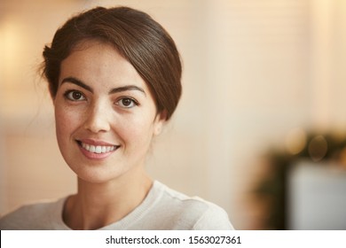 Close up portrait of elegant Middle-Eastern woman smiling at camera while posing in home interior, copy space