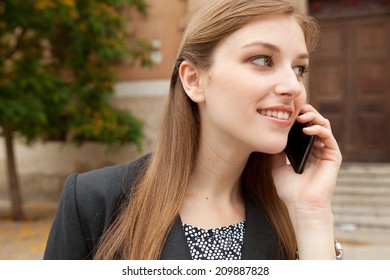 Close Up Portrait Of An Elegant Professional Business Woman Standing In A City Park, Smiling And Having A Phone Call Conversation With Her Smartphone Device. Business Technology Outdoors.