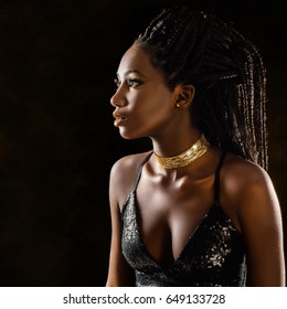 Close up portrait of elegant young african woman in party dress. Low key close up studio shot of girl with long braided hair against dark background.