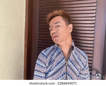 Close up portrait of Emerging artist, fashion designer. Androgynous asian Boy wearing pattern decorative blouse against  Wood Door Partition.  that also a person with skoliosis. Unique Person - Powered by Shutterstock