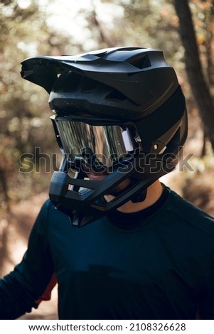 Close up of Portrait of enduro mtb or downhill mtb rider on mountain trail. Black full face helmet, goggles, blue gloves and cycling gear in the forest in winter.