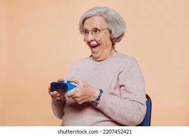Close up portrait of excited elder grandmother with toothy smile playing video game at studio isolated over beige background. Player, console, gamer concept. - Shutterstock ID 2207452421