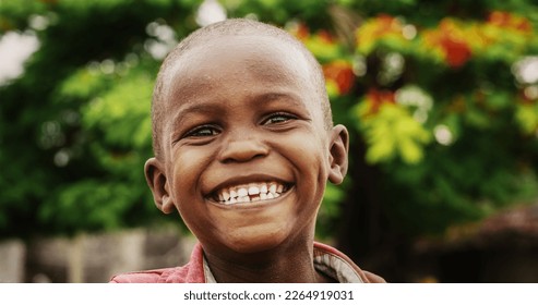 Close Up Portrait of an Expressive Authentic African Kid Laughing and Looking at the Camera Blurry Background. Happy Energetic Black Boy Full of Life Smiling Happily and Enjoying Life and Childhood - Powered by Shutterstock