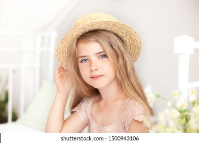 Close Up Portrait Face Of Cute Girl In Straw Hat. Thoughtful Little Blonde With Long Hair Sits On Bed In Bright Children's Room. Childhood Concept. Child Dreams.  Provence Style. Relaxation, Rest