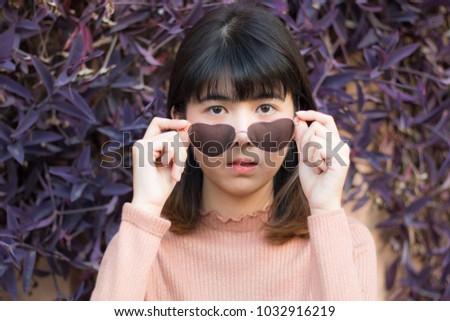 close up portrait face of young beautiful girl wear heart sunglasses . perfect skin of adult asian model posing . pretty lady fashion style . purple flower background