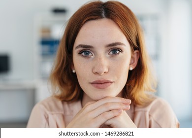 Close Up Portrait Of The Face Of A Young Woman With Shoulder Length Auburn Red Hair Resting Her Chin On Her Hands Staring Thoughtfully At The Camera