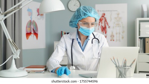 Close Up Portrait Of Female Doctor Wearing Protective Mask And Cap Working With Laptop Computer.