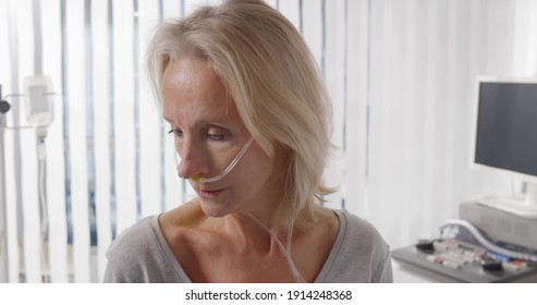 Close Up Portrait Of Female Patient With Nasal Cannula Staying In Hospital Room Alone. Exhausted And Tired Sick Woman With Breathing Tube Sitting In Hospital Ward