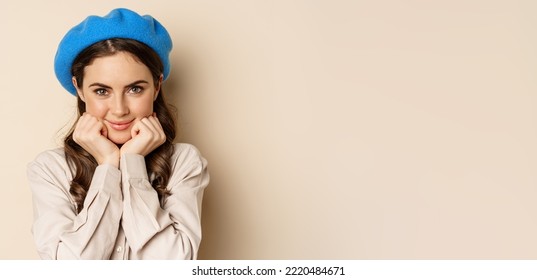 Close Up Portrait Of Feminine Young Woman In Trendy French Hat, Posing Cute And Romantic, Making Silly Coquettish Face And Tender Smile, Beige Background.