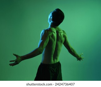 Close up portrait of fit asian male model, shirtless with muscles.  gestural ti chi inspired posing with arms reaching out  Isolated on a moody dark green studio background with silhouette. - Powered by Shutterstock