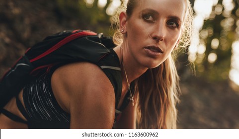 Close Up Portrait Of Fit Woman In Sportwear Wearing Hydration Pack Sitting Outdoors And Looking Away. Mountain Trail Runner Resting After A Run.