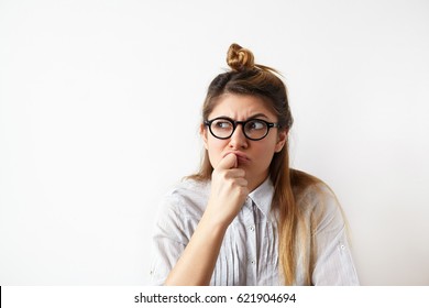 Close up portrait of funny confused woman in glasses thinking and looking aside standing on white wall background. Copy space on the side. Human expressions, emotions, feelings, body language