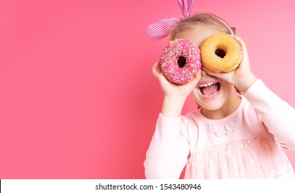 Close Up Portrait Of A Funny Girl With Long Hair Having Fun With Colorful Donuts Against Her Eyes. Satisfied Child With A Bandage On His Hair, Showing Tongue. Expressions, Diet Concept, Vibrant Colors