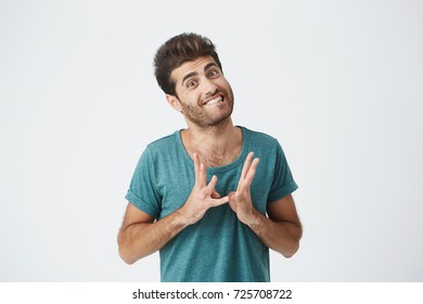 Close Up Portrait Of Funny Stylish Spanish Guy In Blue Tshirt, Biting Lips And Gesticulating With Hands Expressing Feeling Super Awkward. Body Language.