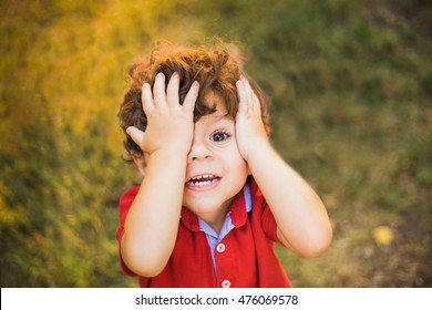 Close Up Portrait Of Funny Toddler Boy Playing Outdoors On Sunny Summer Evening. Sunset Portrait Of Cute Little Child Covering His Face With Hands While Playing Hide And Seek. Top View.