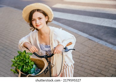 Close up portrait of funny young woman in straw hat with cute smile emotion on her face holding on bicycle outdoor with crosswalk on background.