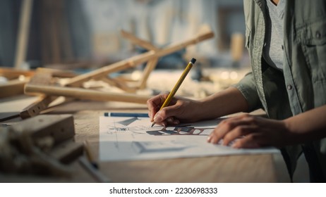 Close Up Portrait of a Furniture Designer Writing Down Dimensions and Assembling Legs of a Wooden Chair. Stylish Black Female Carpenter Working in Studio in Loft Space with Tools on the Walls. - Powered by Shutterstock