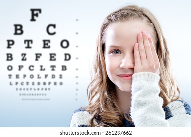 Close up portrait of girl reviewing eyesight closing eye with hand.Out of focus test chart in background.