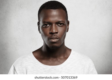 Close up portrait of good-looking serious African man with healthy clean skin wearing white casual t-shirt posing isolated against gray studio wall with copy space for your promotional content - Powered by Shutterstock