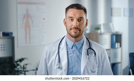 Close Up Portrait Of Handsome Caucasian Professional Medical Doctor Standing In His Health Clinic Office. Successful, Confident Physician In White Coat Looks At The Camera, Smiles In Hospital