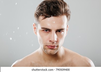 Close up portrait of a handsome half naked man surrounded by water drops isolated over gray background