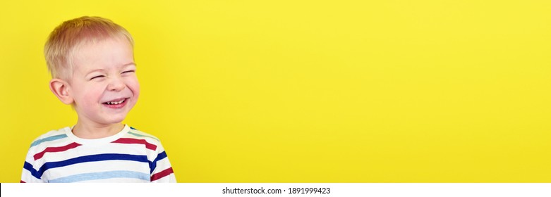 Close Up Portrait Of A Handsome Little Laughing Boy. Adorable Small Child Laughs On Yellow Background. Cute Blonde Kid Smiling And Laughing.