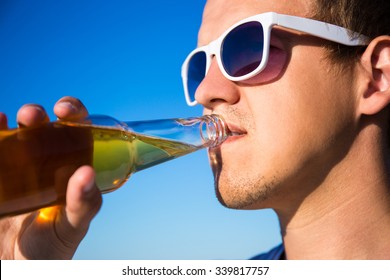 Close Up Portrait Of Handsome Man Drinking Beer Over Sky Background