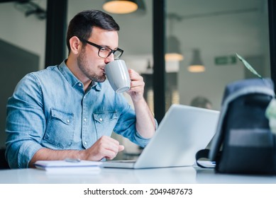 Close up portrait of handsome man working on computer laptop from home office drinking coffee taking break casual entrepreneur small business owner focused doing research holding coffee cup - Shutterstock ID 2049487673