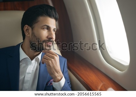 Close up portrait of handsome pensive arab businessman planning project sitting on airplane looking at window. Rich confident entrepreneur flying luxury private jet, successful business concept
