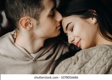 Close up portrait of handsome young couple sitting in a chair where boy with closed eyes is trying to kiss his girlfriend on forehead while she is smiling with closed eyes to. - Powered by Shutterstock