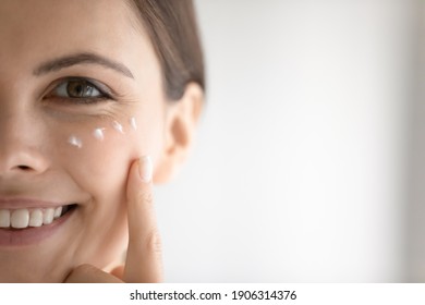 幸せな美しい2000年生のコーカサスの女性の接写は、シワにアンダークリームを塗りつぶしています。 笑顔の若い女性は、肌に保湿剤を使います。 スキンケアのコンセプト。