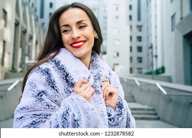 Close Up Portrait Of Happy Beautiful Young Cute Woman In Vegan And Faux Fur Coat Is Posing On Urban City Background. Fashion Trendy Style Clothes