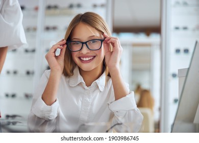 Close up portrait of happy cheerful female child wearing eyeglasses while sitting in optician center