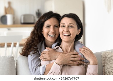 Close up portrait happy different age women hugging at home. Beautiful Hispanic female cuddling tightly her mature mother, laughing, looking at camera enjoy time together, showing strong family ties - Powered by Shutterstock