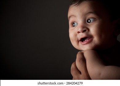 Close Up Portrait Of A Happy Indian Baby Boy Laughing In Fathers Arms Over Dark Gray Background