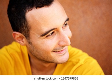 Close Up Portrait Of Happy Latin Man Looking Away Against Brown Background