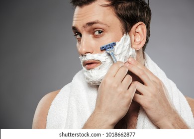 Close Up Portrait Of Happy Man Looking On Camera And Shaving His Face With Razor Isolated Over Gray Background