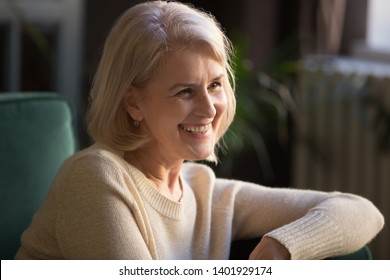 Close Up Portrait Of Happy Mature Blond Woman Having Candid Smile Looking Away, Attractive Middle Aged Female Sit On Sofa Feels Satisfied Spend Time At Home, Old Natural Beauty Healthy Retiree Concept