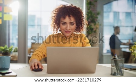 Close Up Portrait of a Happy Middle Eastern Manager Sitting at a Desk in Creative Office. Young Stylish Female with Curly Hair Using Laptop Computer in Marketing Agency.