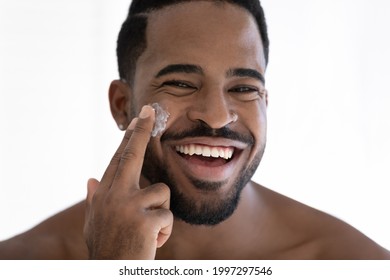 Close up portrait of happy mixed race Black guy applying collagen cream on face, moisturizing, skin, cleansing pores with lotion, putting sunscreen for protection from sun. Skincare concept. Head shot - Powered by Shutterstock