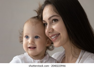 Close Up Portrait Of Happy New Mom And Cute Blue Eyed Baby Girl Enjoying Time Together. Smiling Young Mother Holding Adorable Toddler Kid In Arms, Looking Away. Motherhood, Child Care Concept